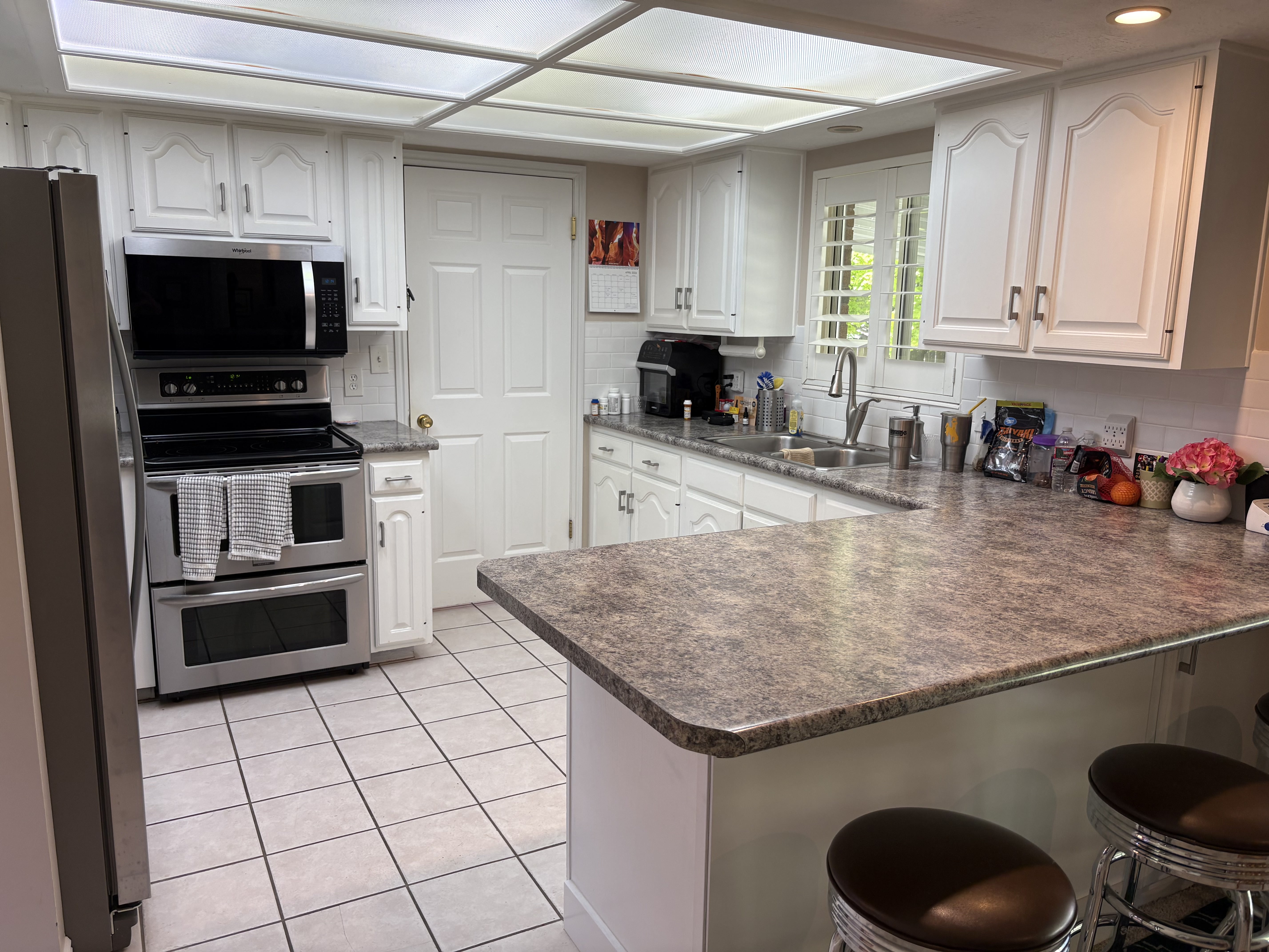 Kitchen featuring white cabinetry, stainless steel appliances, speckled countertops, a tile backsplash, and tile flooring