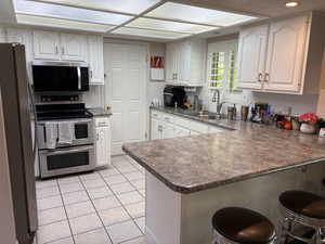 Kitchen featuring white cabinetry, stainless steel appliances, speckled countertops, a tile backsplash, and tile flooring