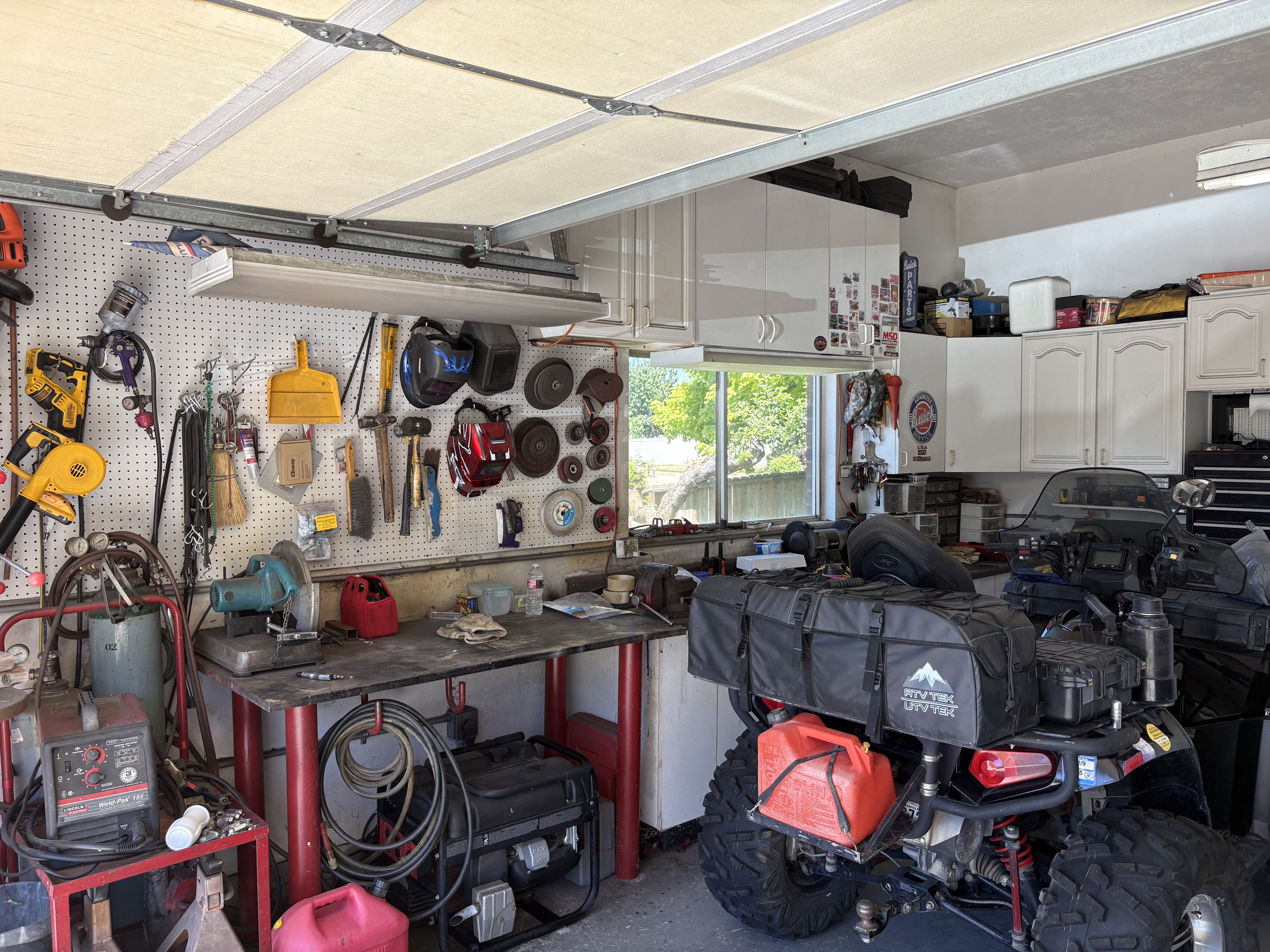 Spacious garage featuring a dedicated workbench area, pegboard storage, overhead fluorescent lighting, a built-in window, and ample cabinet storage