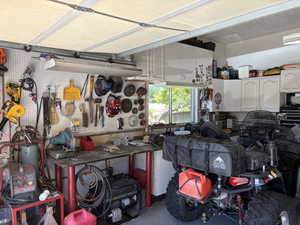 Spacious garage featuring a dedicated workbench area, pegboard storage, overhead fluorescent lighting, a built-in window, and ample cabinet storage