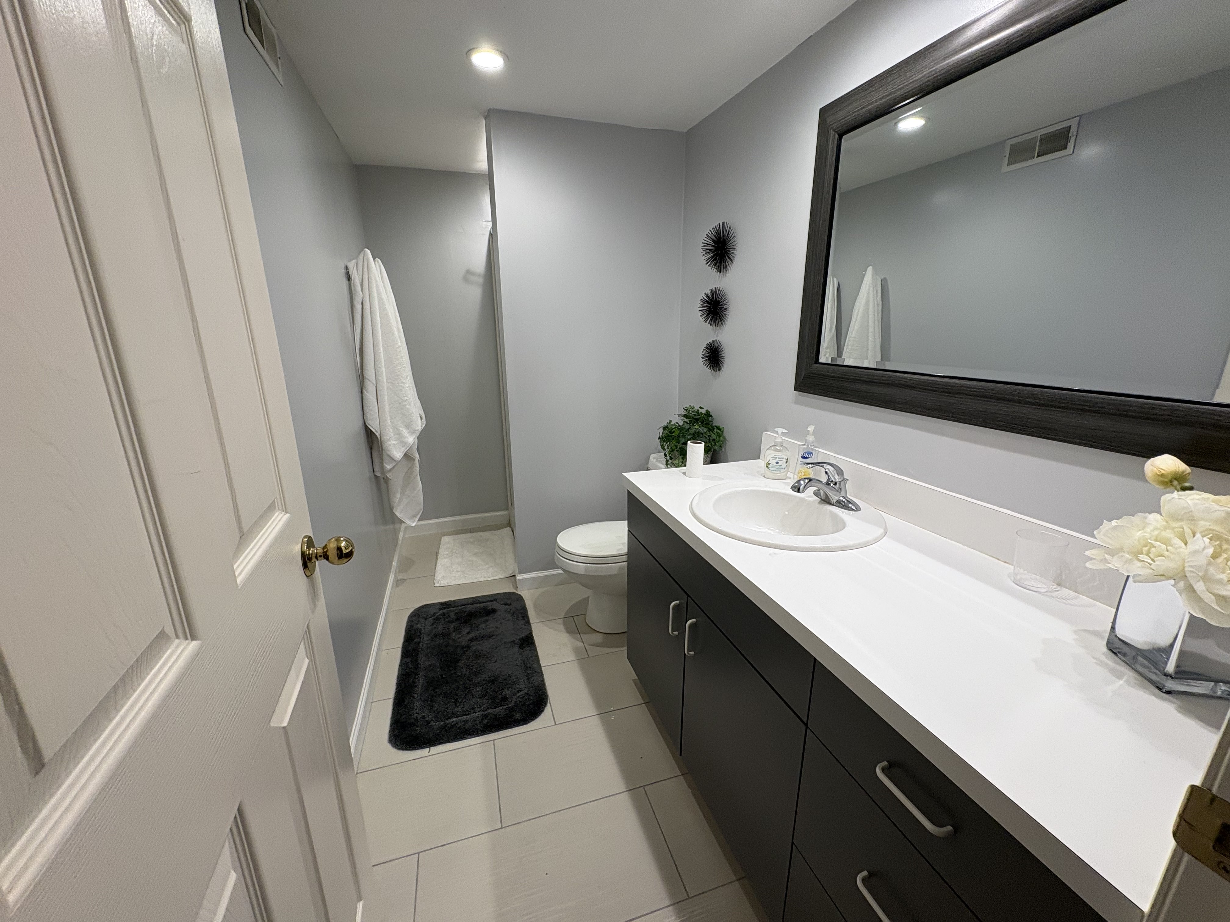 Bathroom featuring a dark wood-finish vanity with a white countertop and integrated sink, a large framed mirror, recessed lighting, and light-toned tile flooring