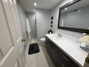 Bathroom featuring a dark wood-finish vanity with a white countertop and integrated sink, a large framed mirror, recessed lighting, and light-toned tile flooring