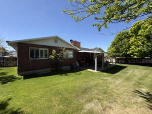 Spacious backyard featuring a covered patio, brick exterior, white vinyl siding, mature perimeter trees, and a wooden fence