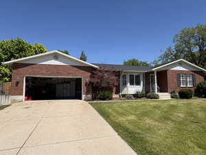 Brick and white siding exterior featuring a two-car garage, mature landscaping, and a concrete driveway