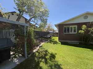 Expansive backyard featuring a manicured lawn, red brick exterior, white soffit and fascia, white window trim with plantation shutters, and a wood privacy fence