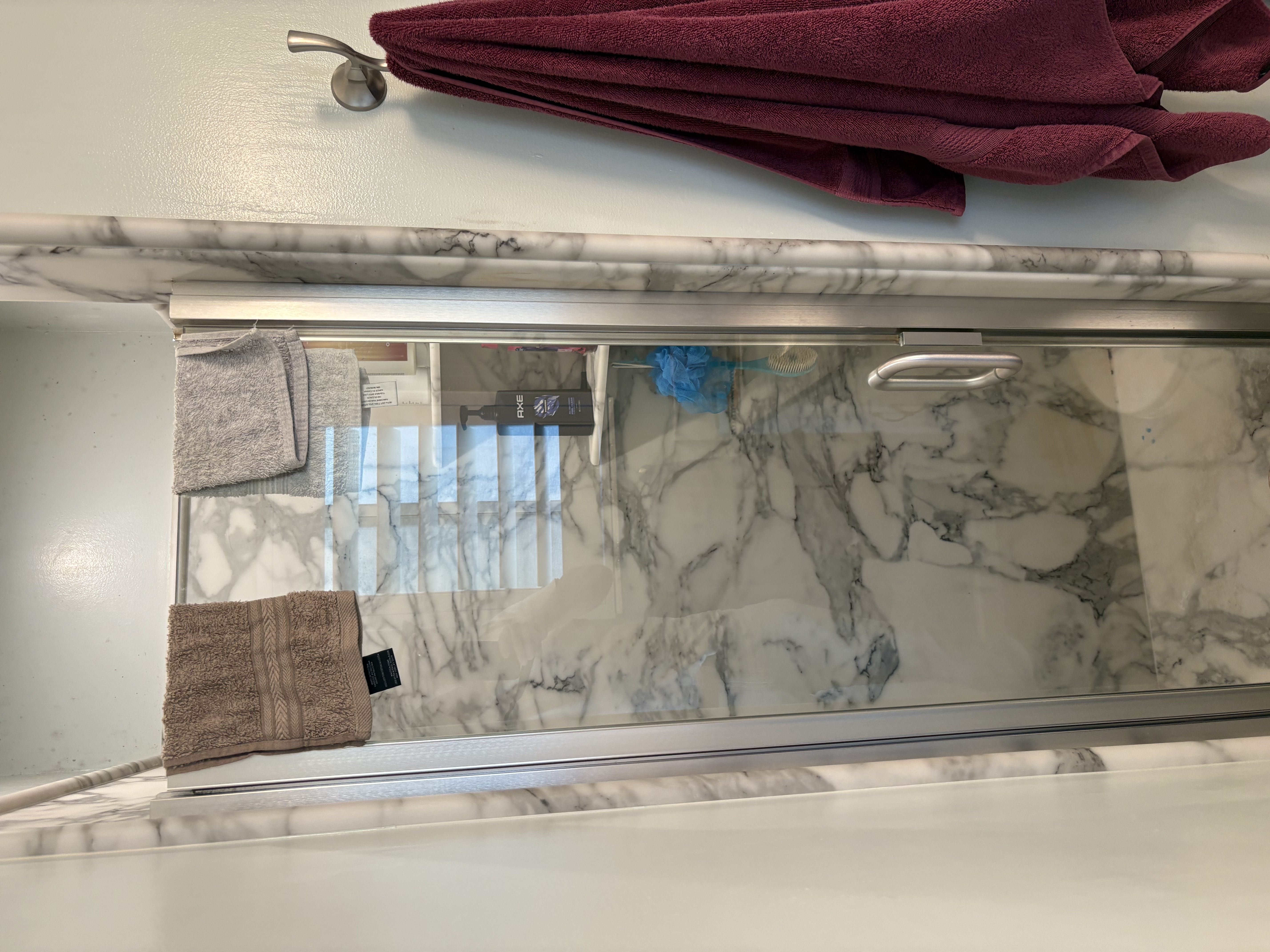 Walk-in shower featuring glass enclosure with a metal handle and frame