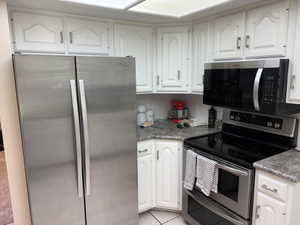 Kitchen featuring white cabinetry, grey countertops, stainless steel side-by-side refrigerator, stainless steel electric range, and stainless steel microwave