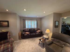 Carpeted living area featuring recessed lighting, a window with plantation shutters, neutral-toned walls, and a doorway to an additional room