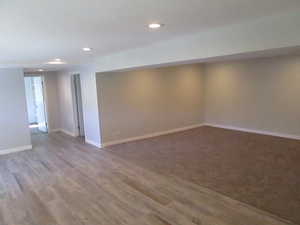 Spacious room featuring light wood-finish flooring, a plush carpeted area, recessed lighting, and neutral wall tones