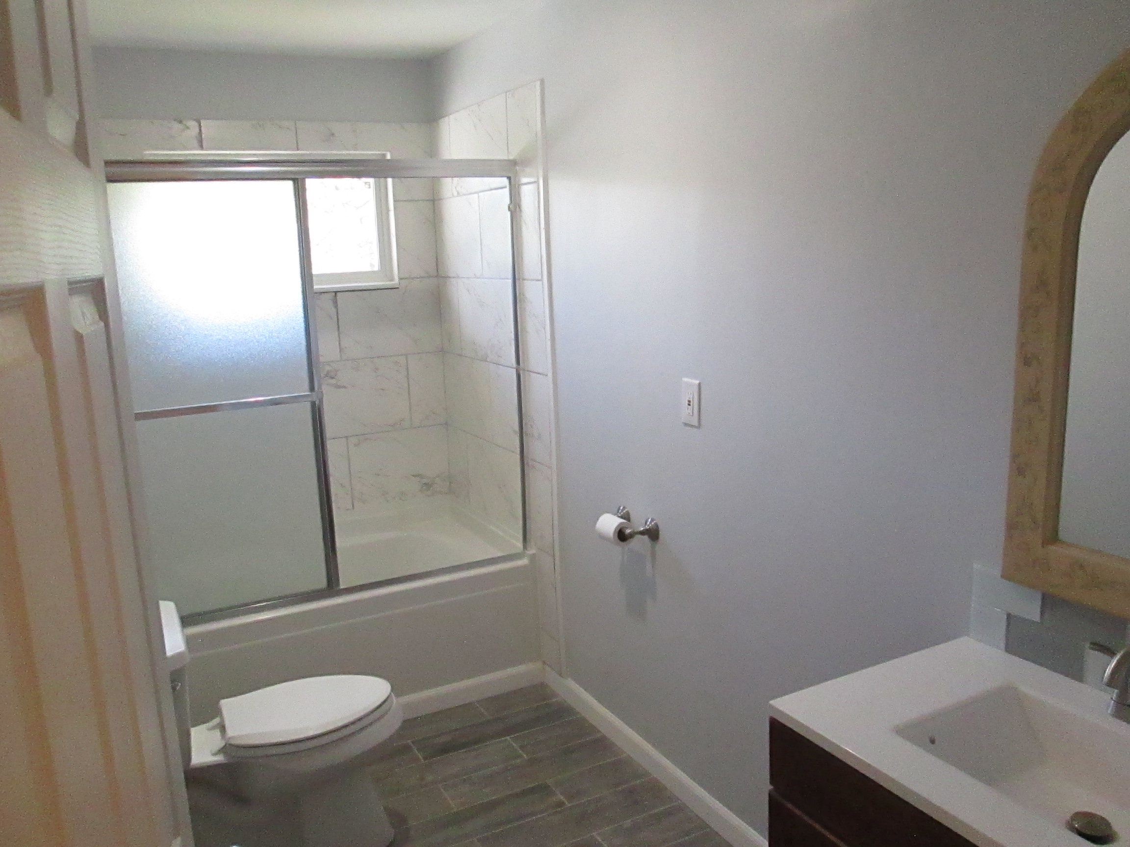 Bathroom featuring a full tub and shower with sliding glass doors, white tiled surround, modern vanity with an integrated sink, and wood-finish flooring