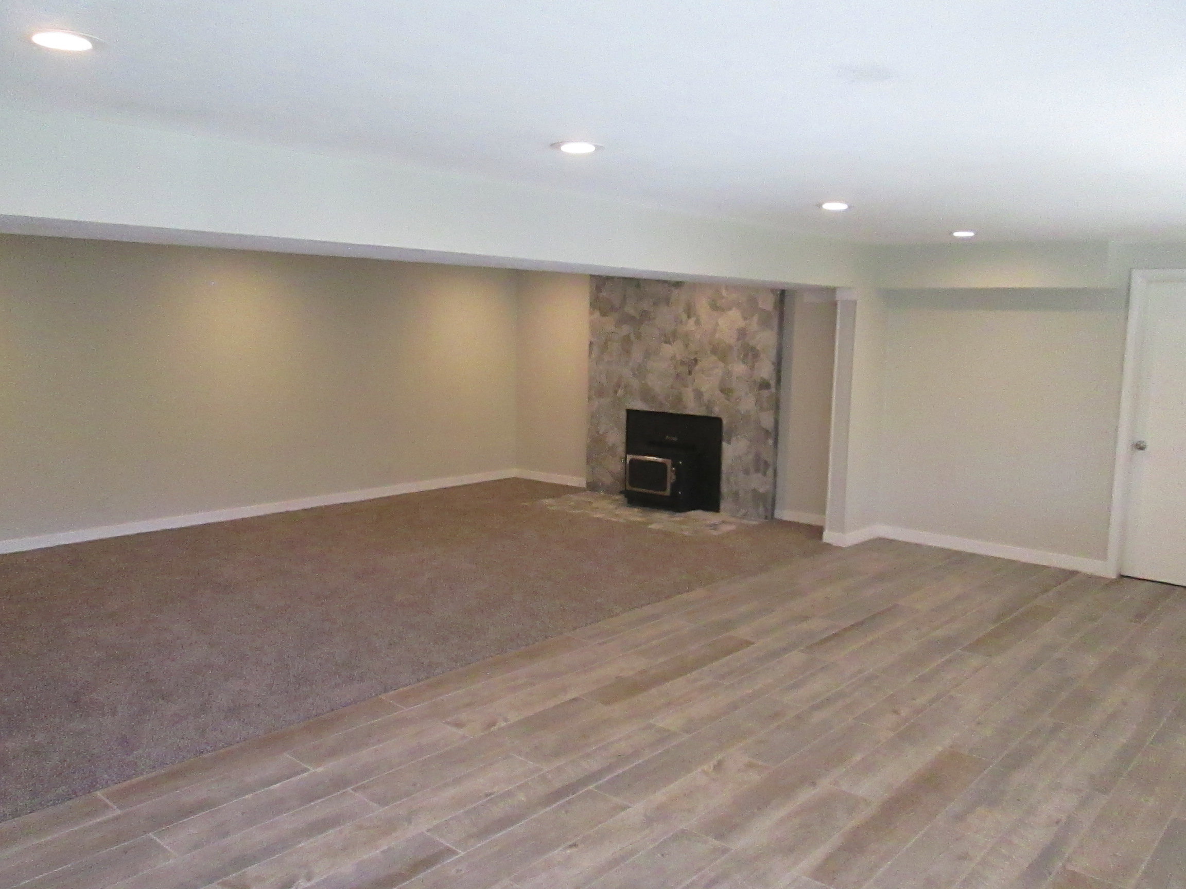 Spacious room featuring recessed lighting, a stone-clad fireplace with a dark insert, and a combination of wood-look flooring and carpeting