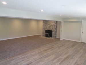 Spacious room featuring recessed lighting, a stone-clad fireplace with a dark insert, and a combination of wood-look flooring and carpeting