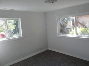Bright interior space featuring two windows, neutral painted walls, white trim, and dark carpet flooring