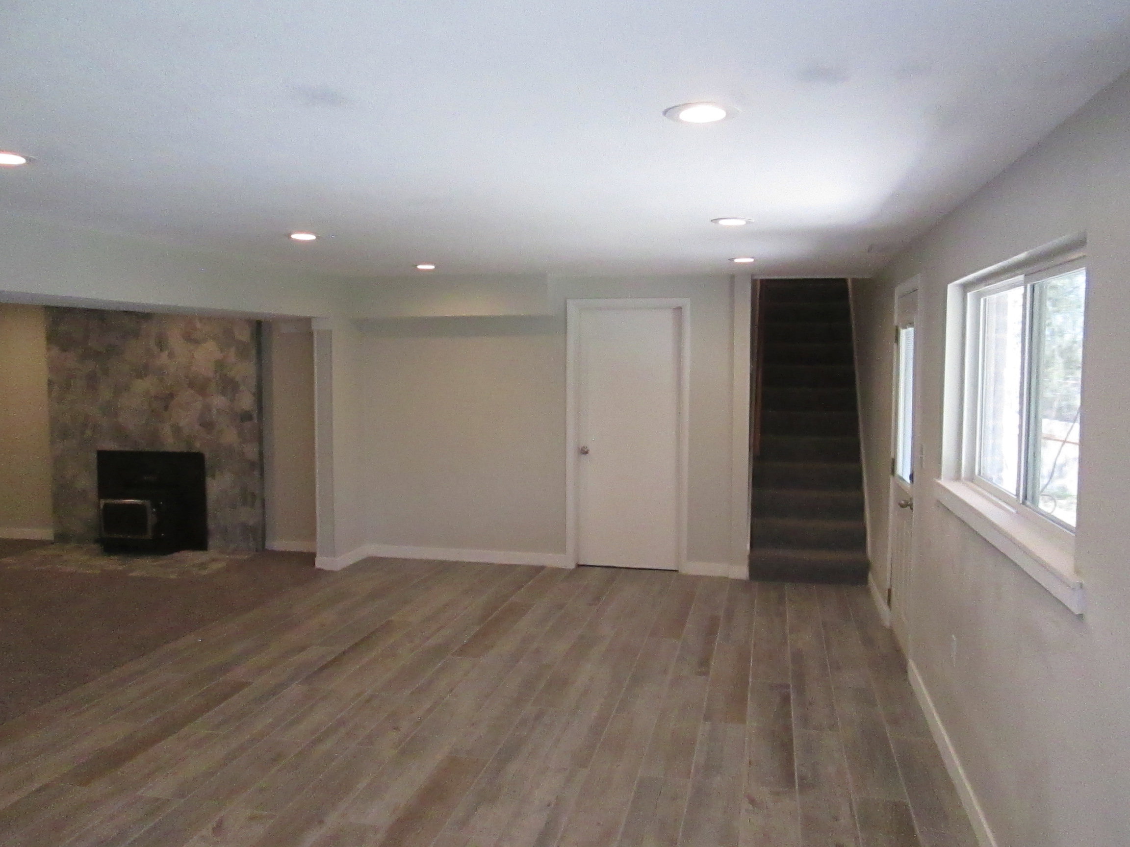 Spacious room featuring wood-finish flooring, recessed lighting, and a stone-clad fireplace with a dark hearth