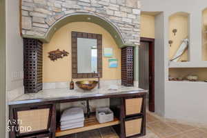 Bathroom vanity featuring an ornate mirror, vessel sink, and stone countertop