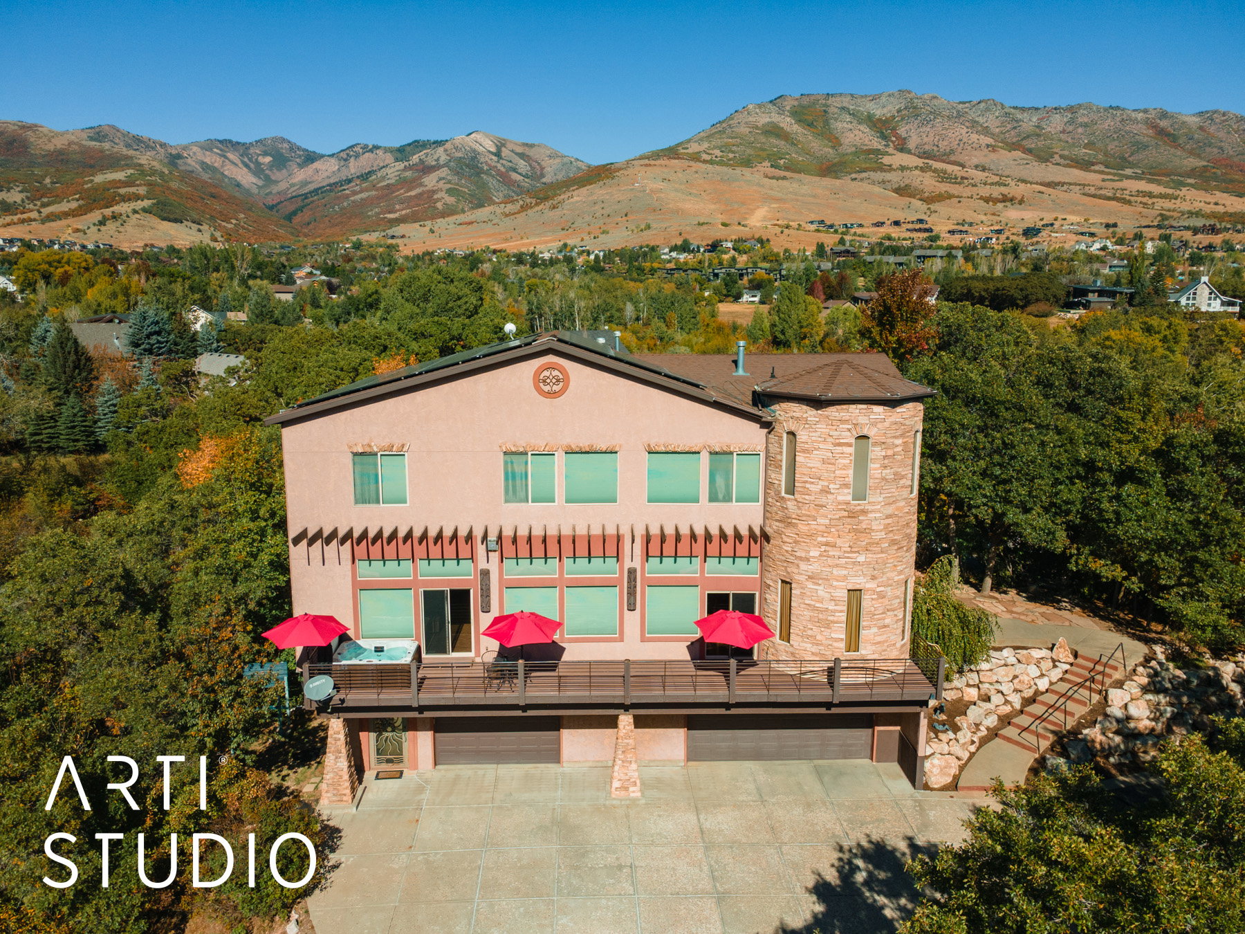 Stucco exterior with stone turret architectural feature, multi-level deck, attached two-car garage, and a concrete driveway