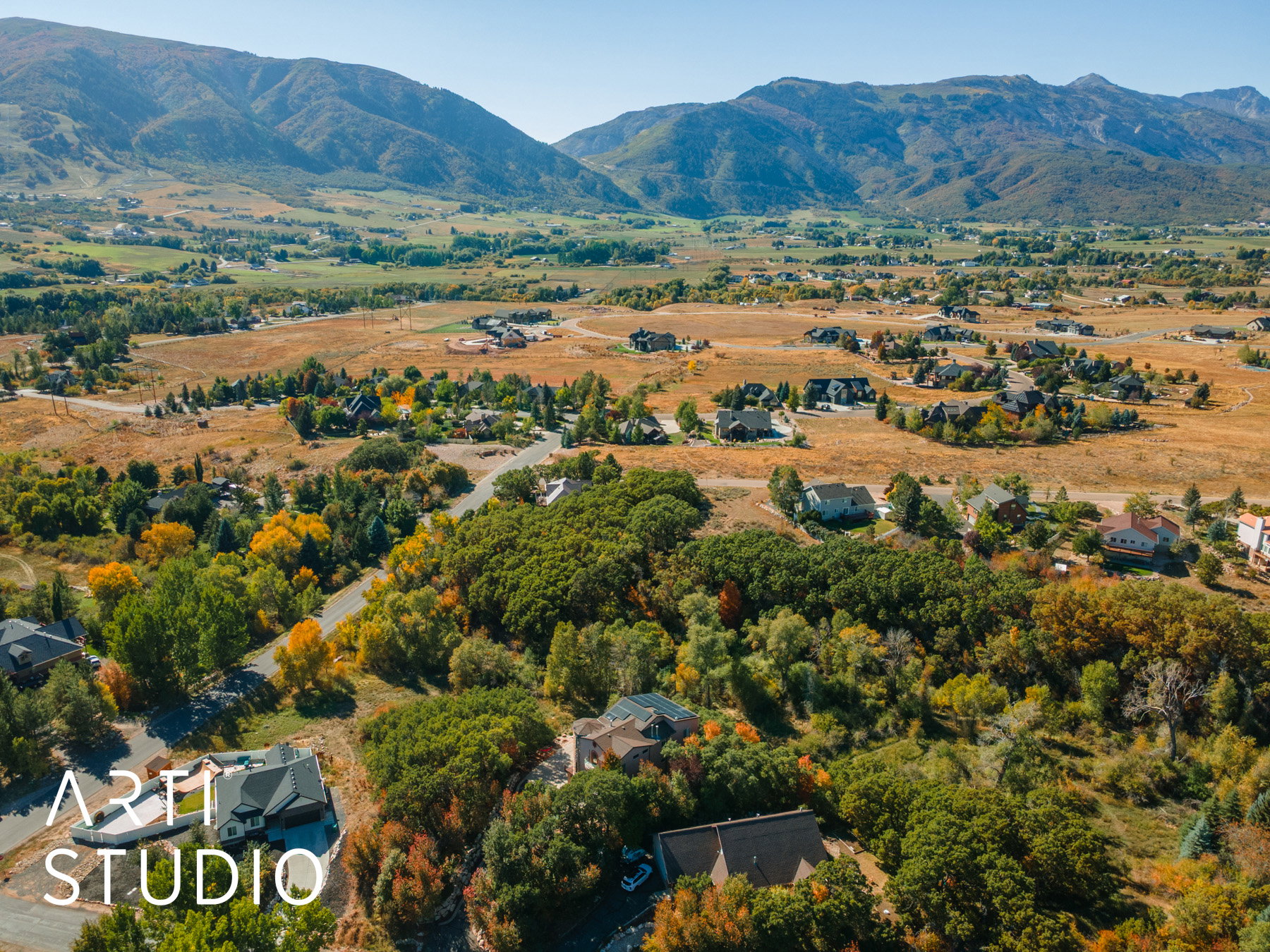 Expansive mountain landscape featuring a valley with residential properties, natural foliage, and distant peaks