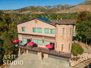 Multi-level stucco exterior featuring a prominent stone-clad turret, solar panels, and a full-width deck with a hot tub