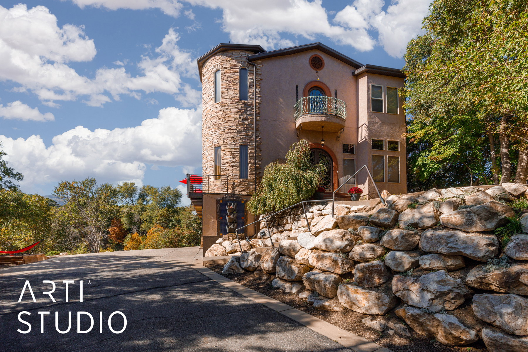 Multi-level stucco residence featuring a stone-clad turret, arched entry, and decorative copper balcony