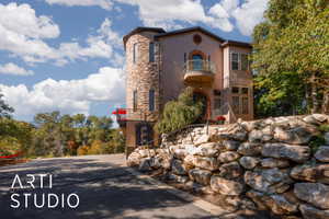 Multi-level stucco residence featuring a stone-clad turret, arched entry, and decorative copper balcony