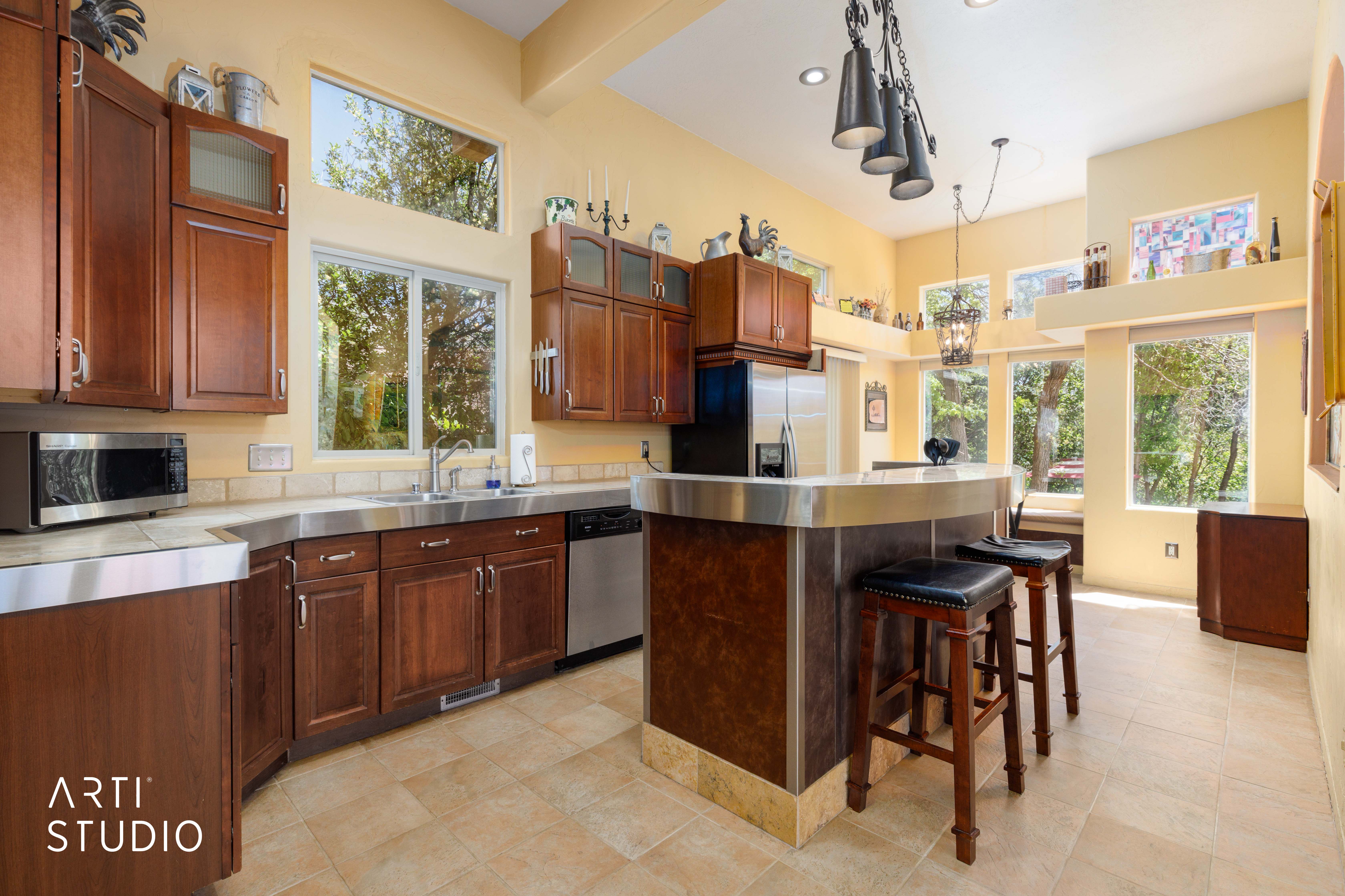 Kitchen featuring stainless steel countertops, wood cabinetry with glass-front accents, and a built-in breakfast bar