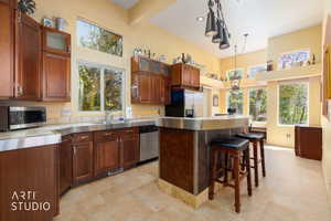 Kitchen featuring stainless steel countertops, wood cabinetry with glass-front accents, and a built-in breakfast bar