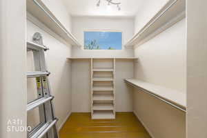 Walk-in closet featuring built-in shelving, hanging rods, an upper window, and track lighting