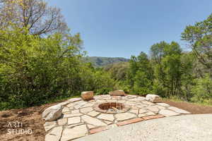 Outdoor fire pit area featuring a natural stone patio and brick fire ring, surrounded by lush trees and distant mountains