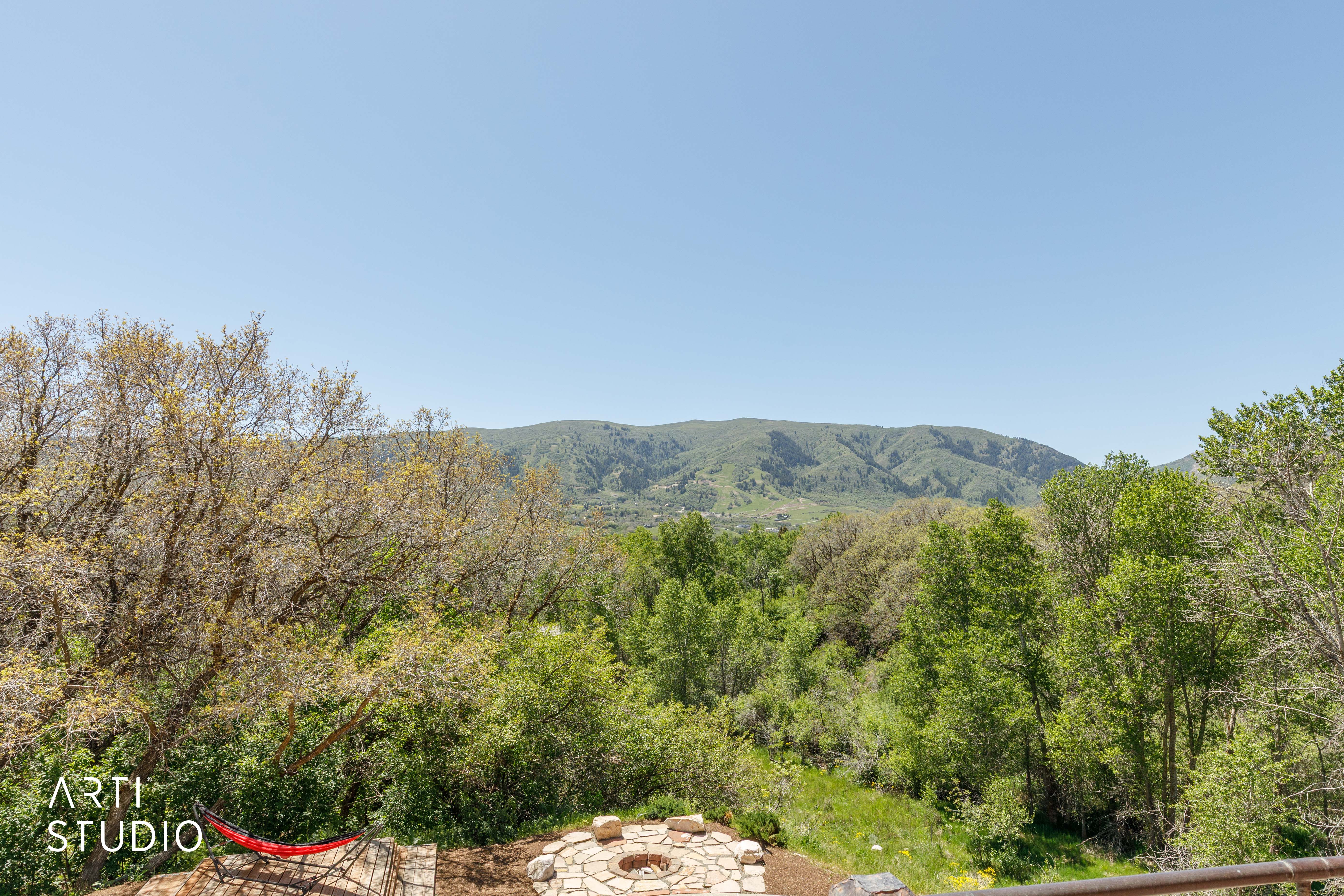 Outdoor fire pit area with stone surround, complemented by a surrounding natural landscape with abundant greenery and distant mountains