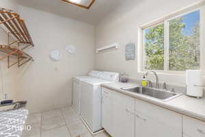 Utility room featuring a large window, a stainless steel sink, white cabinetry, and tile flooring