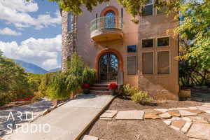 Stucco exterior featuring a stone accent tower, ornate double entry doors, a curved balcony with decorative copper, and a concrete walkway with flagstone detailing