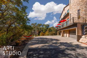 Stone-clad exterior featuring multiple balconies with metal railings, a ground-level garage, and mature trees surrounding a paved driveway