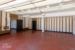 Spacious garage featuring a red speckled epoxy floor, white walls with wood-panel accents, two dark paneled doors, and exposed ceiling beams