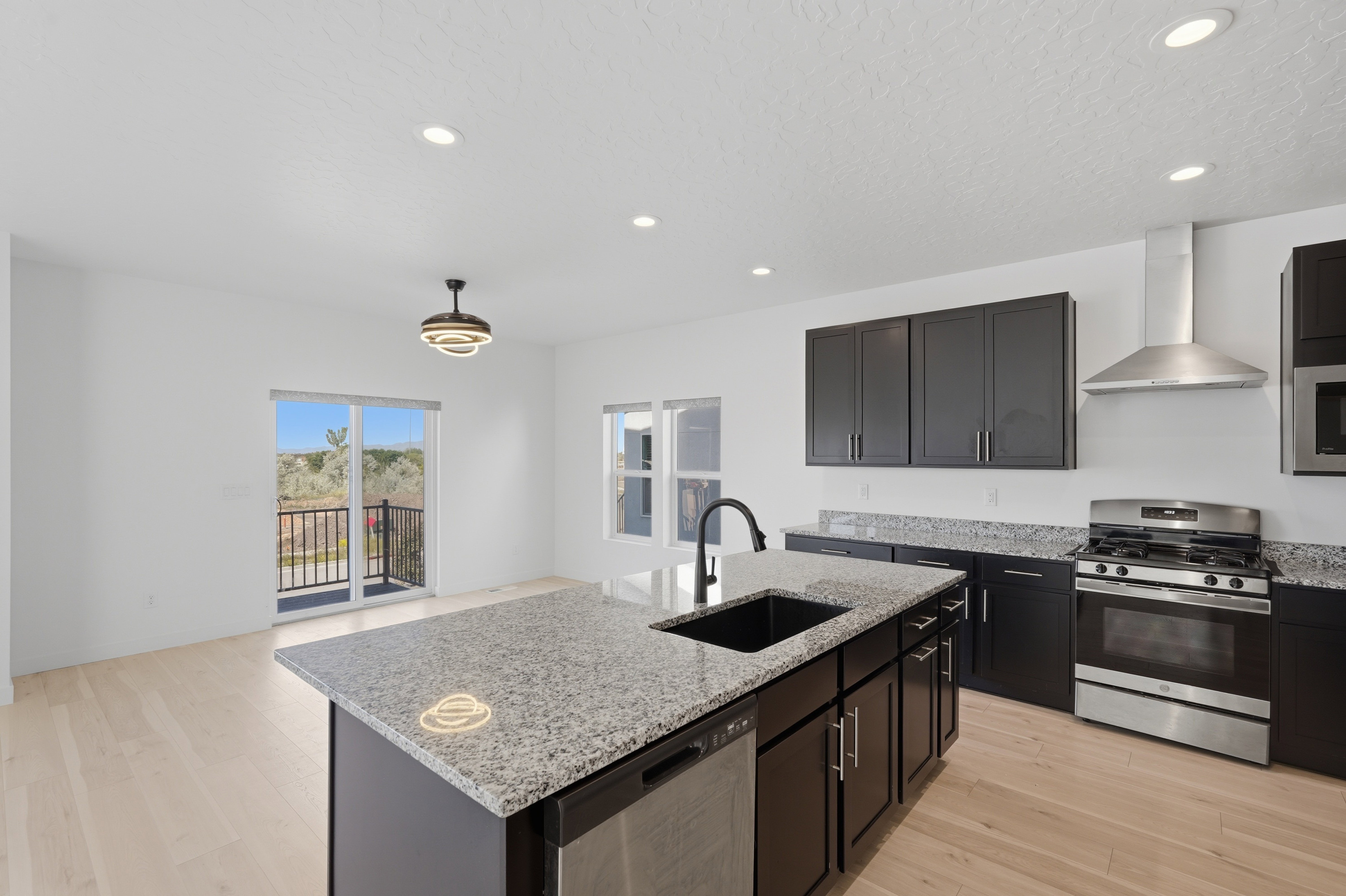 Open-concept kitchen featuring an island with granite countertops and an undermount sink, dark wood-finish cabinetry, stainless steel appliances, and light wood-finish flooring