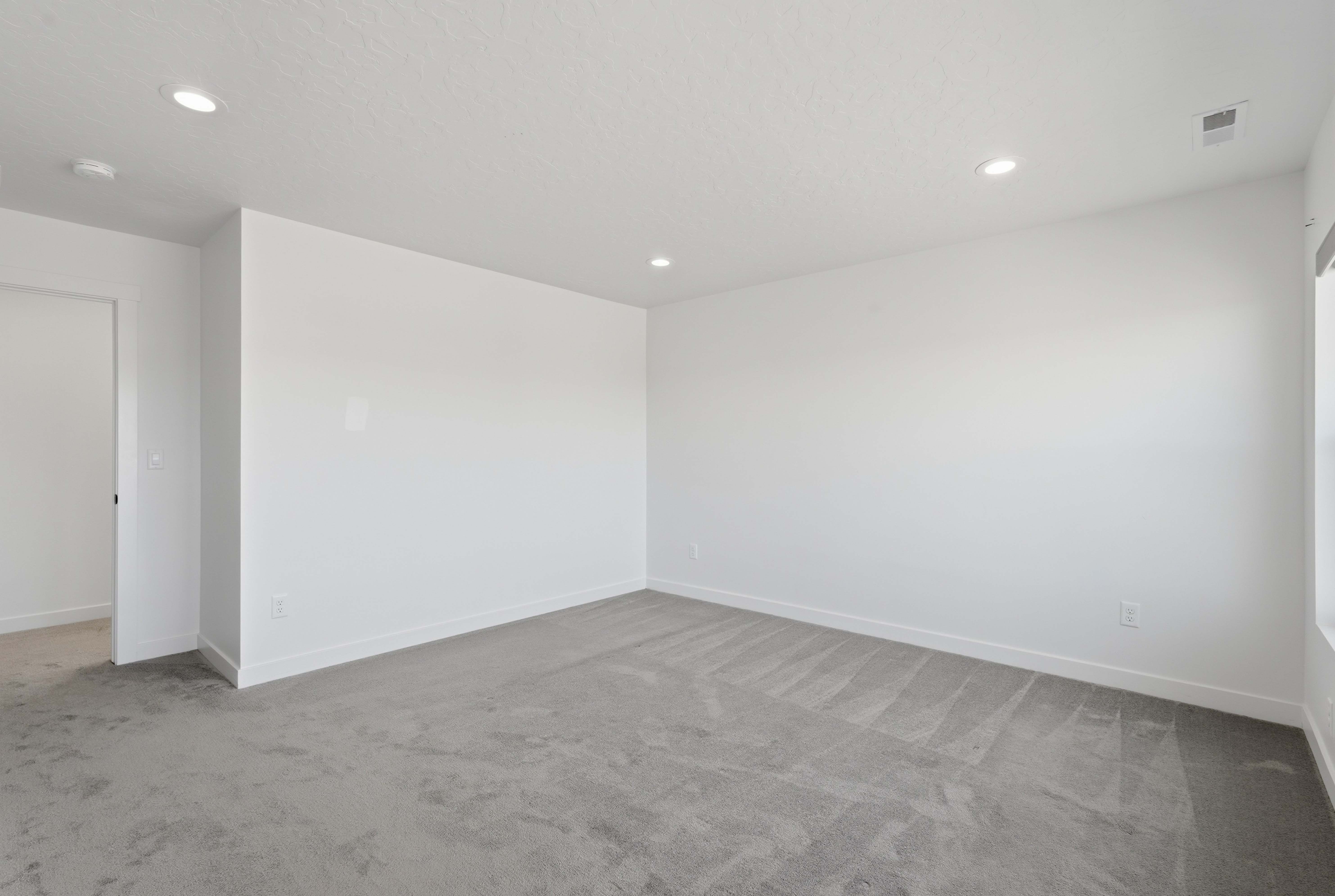 Spacious interior room featuring light gray carpeting, white walls, recessed lighting, and white baseboards