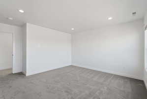 Spacious interior room featuring light gray carpeting, white walls, recessed lighting, and white baseboards