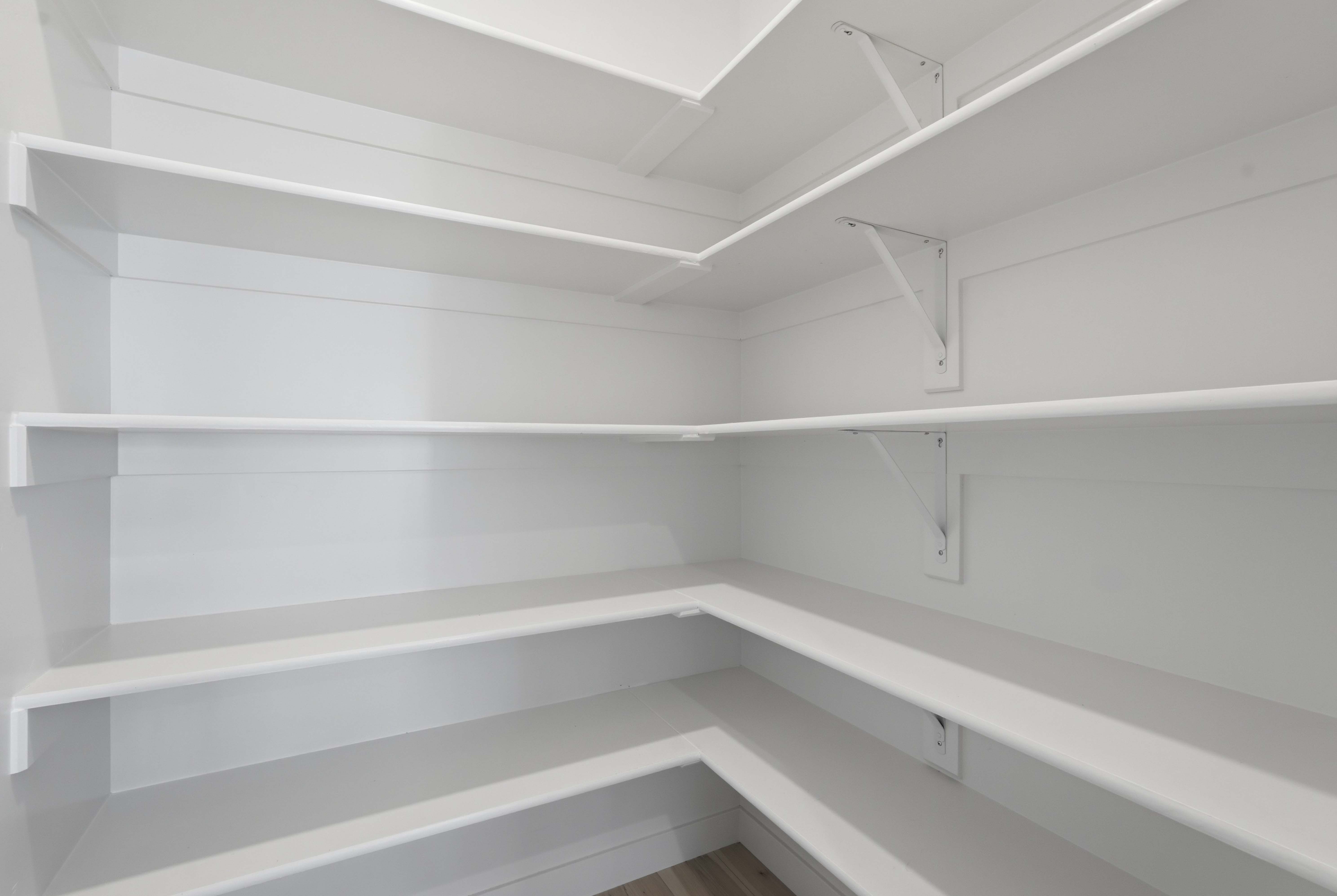Expansive pantry featuring multiple levels of white shelving, support brackets, and wood-finish flooring