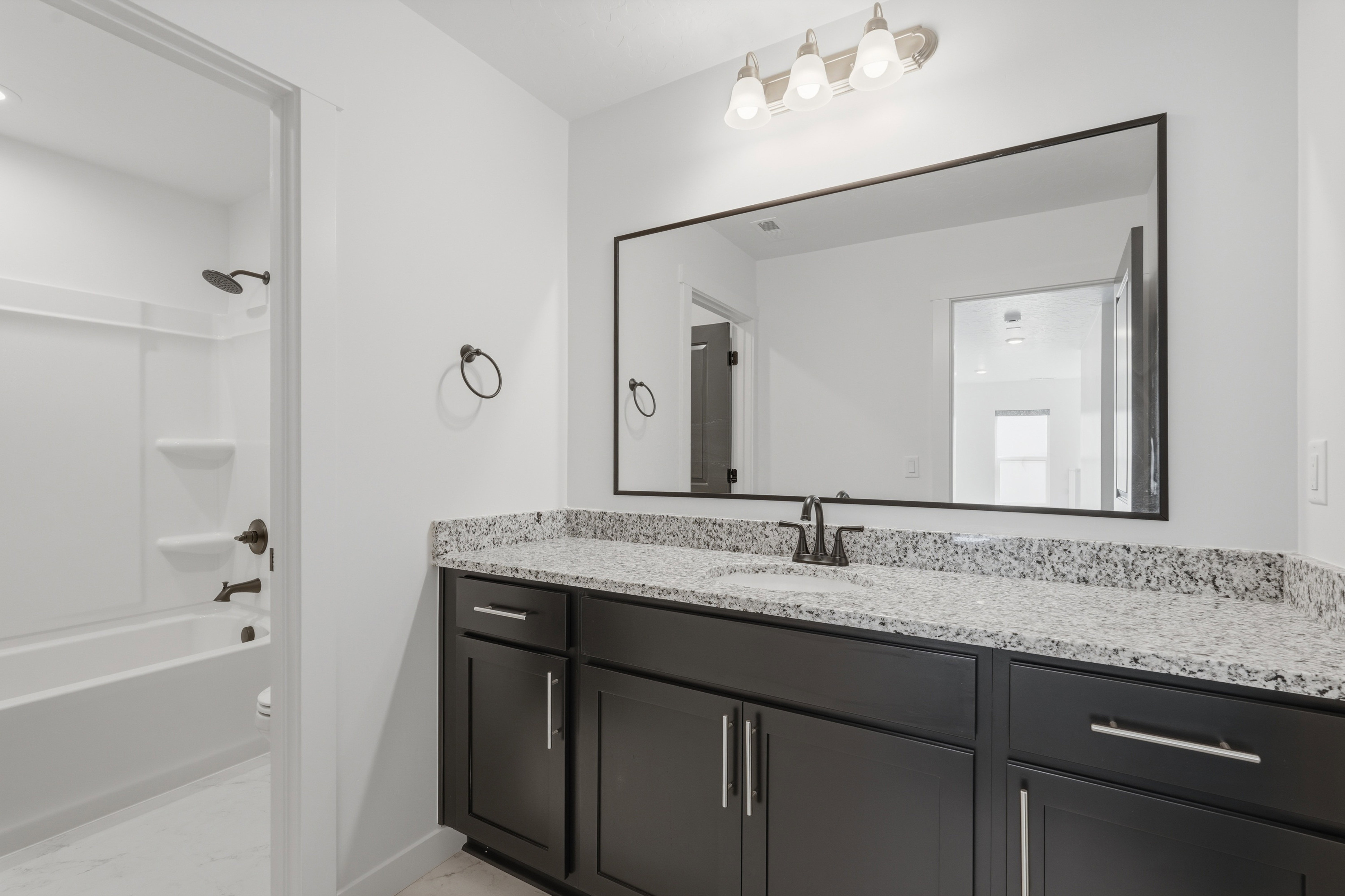 Bathroom featuring a spacious vanity with black cabinetry, a light speckled countertop, and a large framed mirror