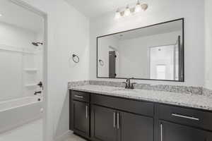 Bathroom featuring a spacious vanity with black cabinetry, a light speckled countertop, and a large framed mirror
