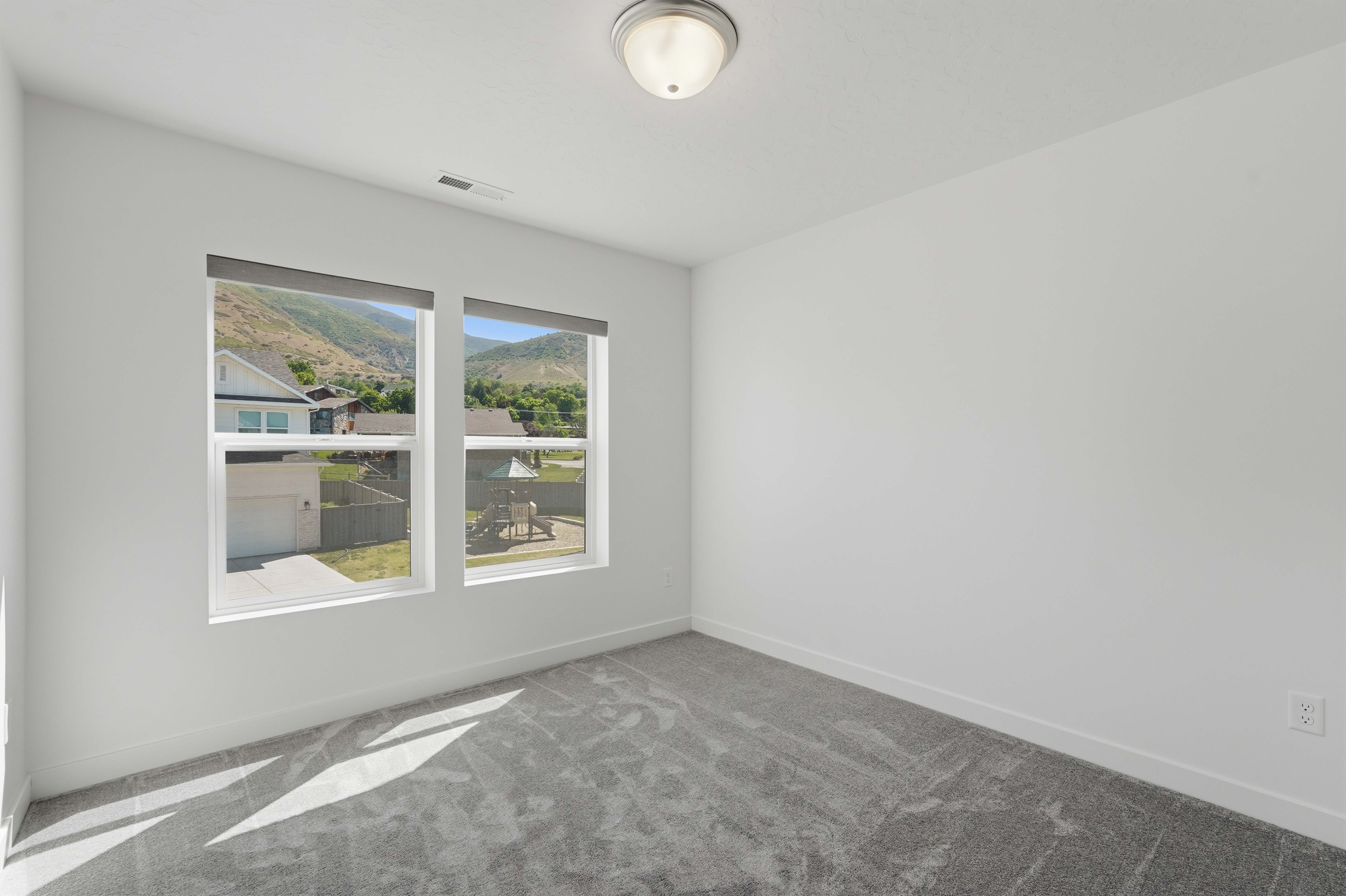 Bright interior space featuring two large windows, roller shades, white walls, gray patterned carpet, and a flush mount ceiling light