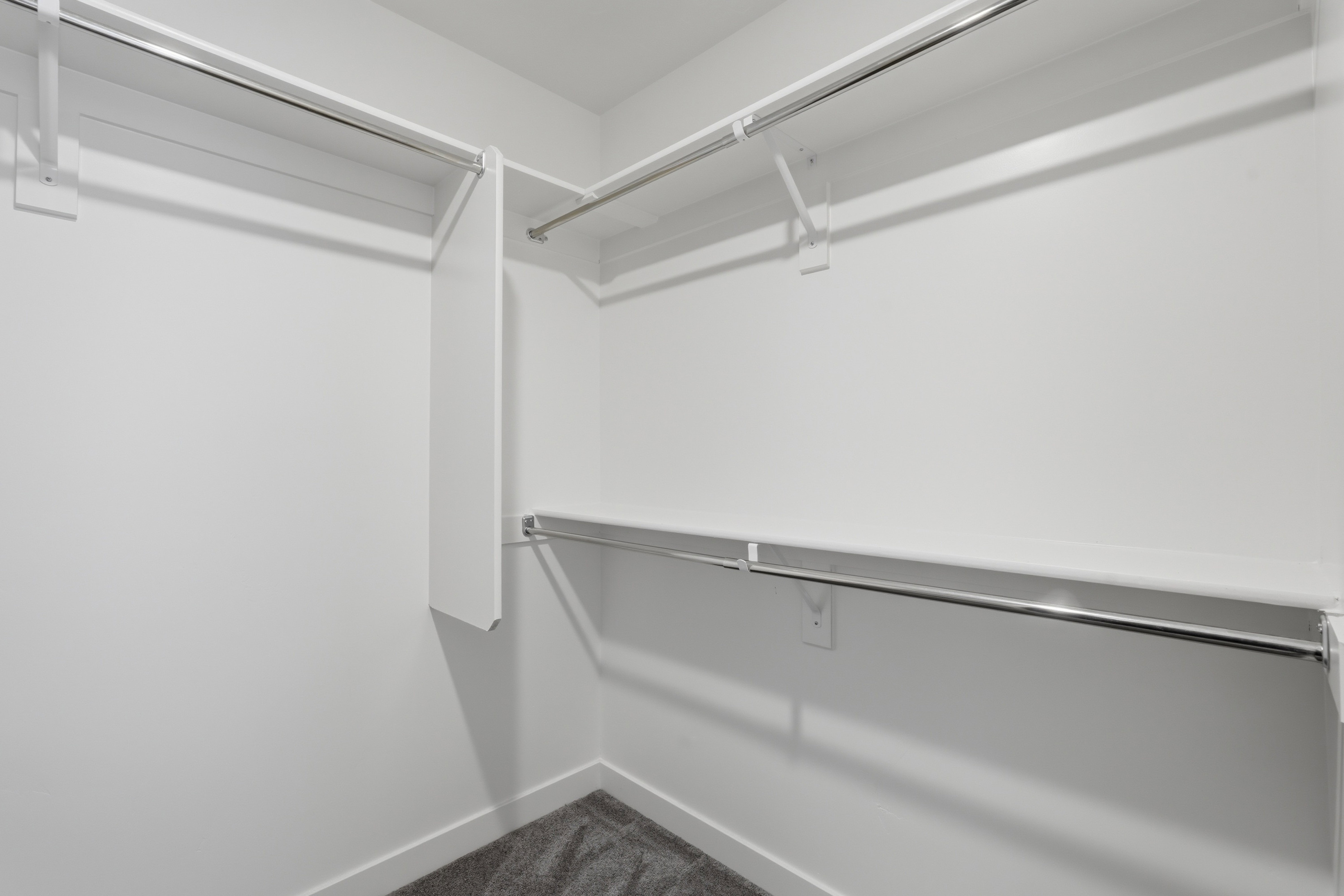 Walk-in closet with white walls, white shelving, and chrome hanging rods