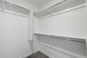 Walk-in closet with white walls, white shelving, and chrome hanging rods