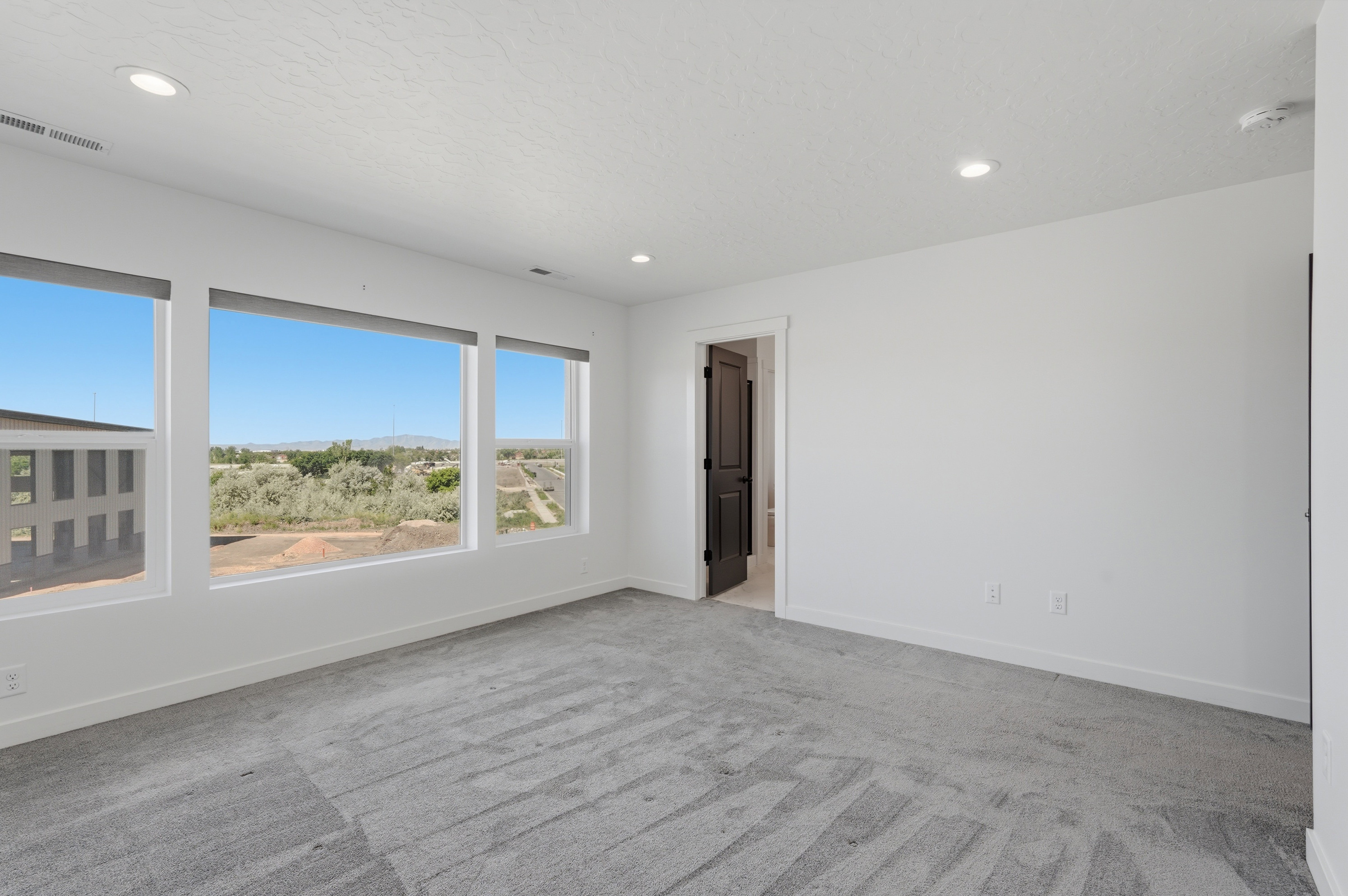 Spacious room featuring three large windows, recessed lighting, and grey patterned carpeting