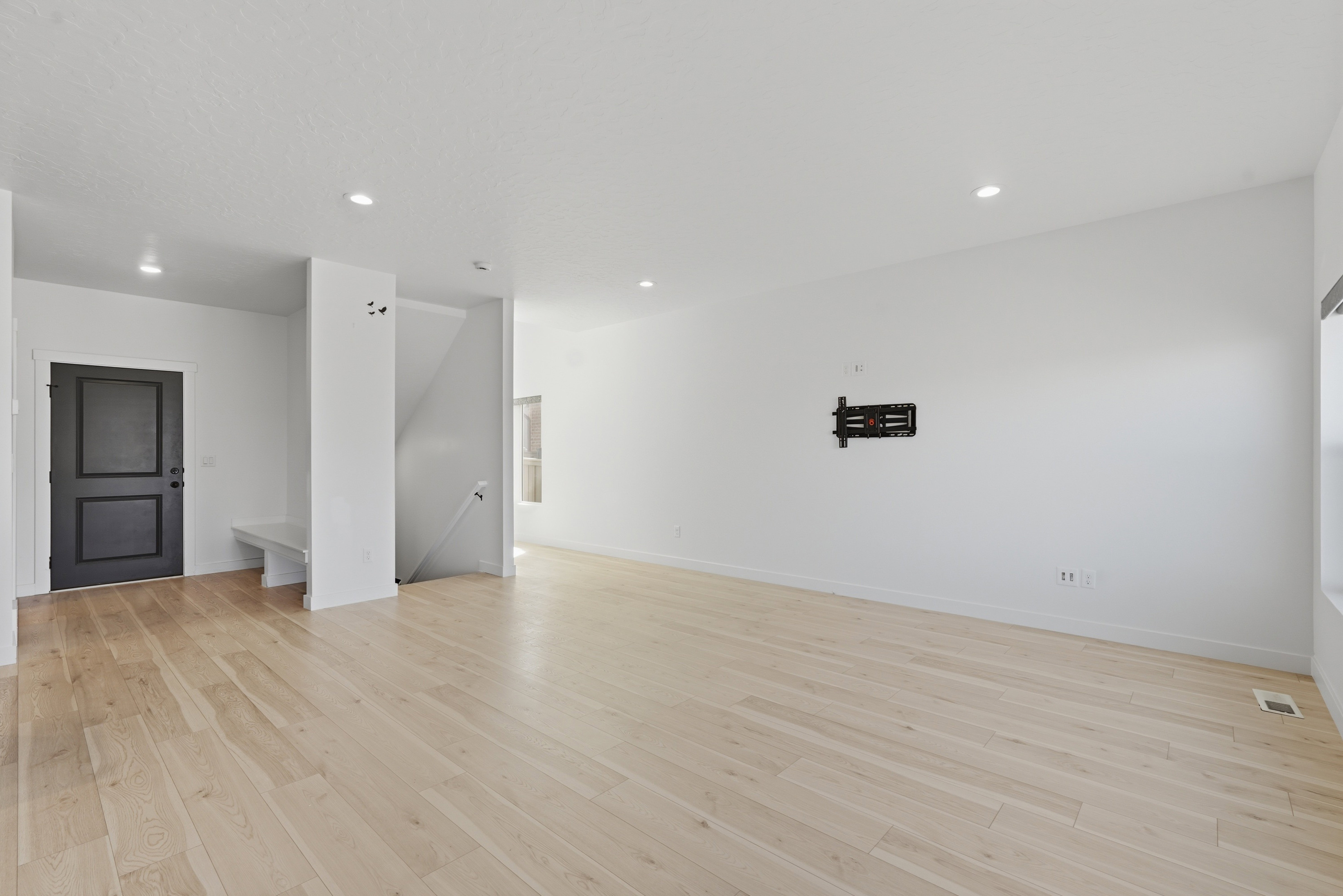 Open-concept living area featuring light wood-finish flooring, recessed lighting, a built-in entry bench, and a dark paneled entry door