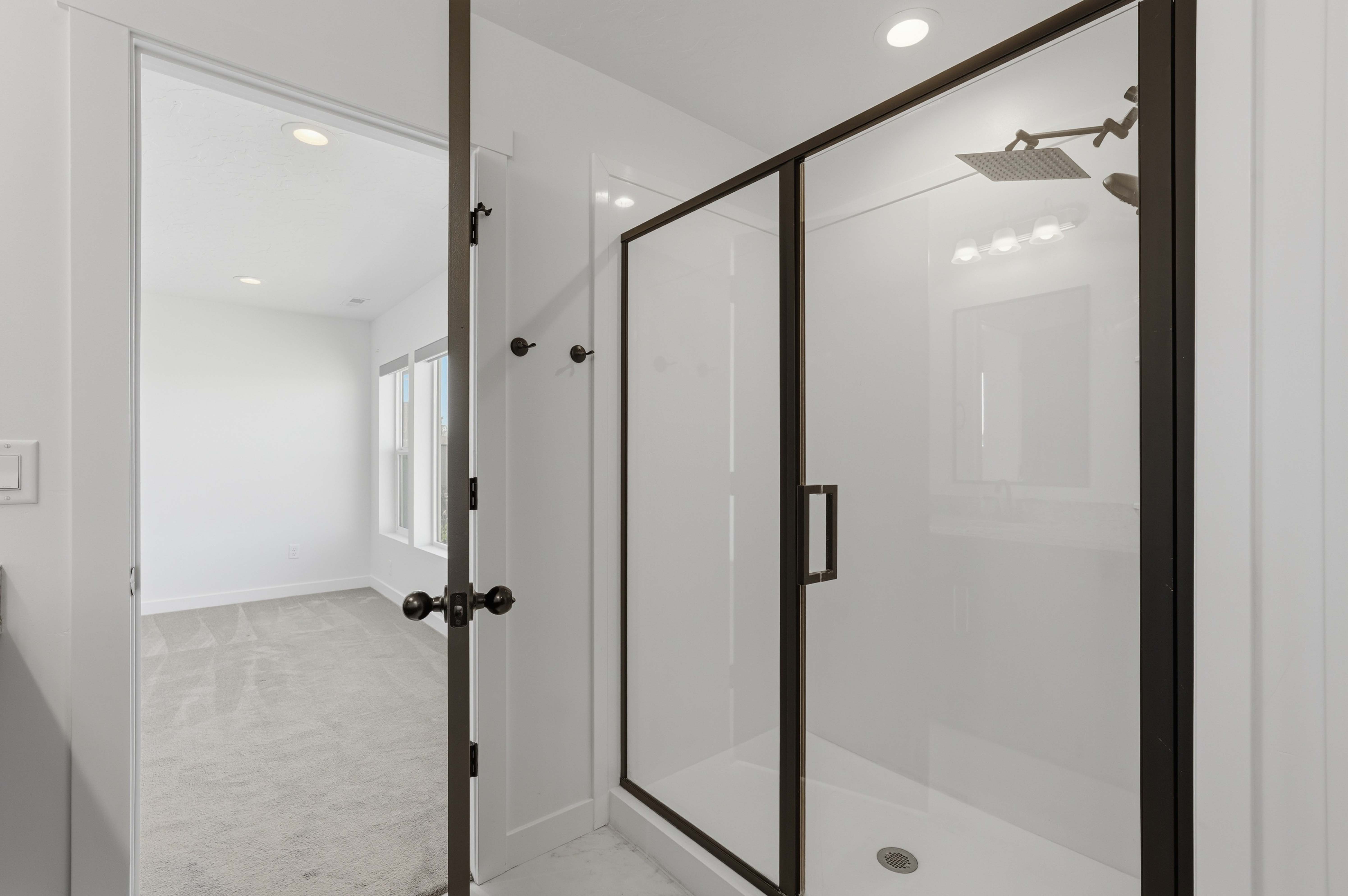 Walk-in shower with dark-framed glass enclosure, square rain shower head, and recessed lighting