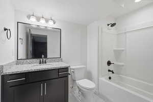 Full bathroom featuring a dark wood-finish vanity with a light speckled countertop, matte black fixtures, a framed mirror, and a full tub with shower