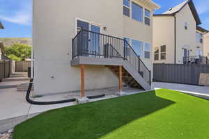 Rear exterior featuring a composite deck with black metal railings, a sliding glass door, multiple large windows, and a lower-level patio with artificial turf