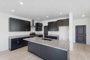Modern kitchen featuring dark cabinetry, speckled countertops, stainless steel appliances, and wood-finish flooring
