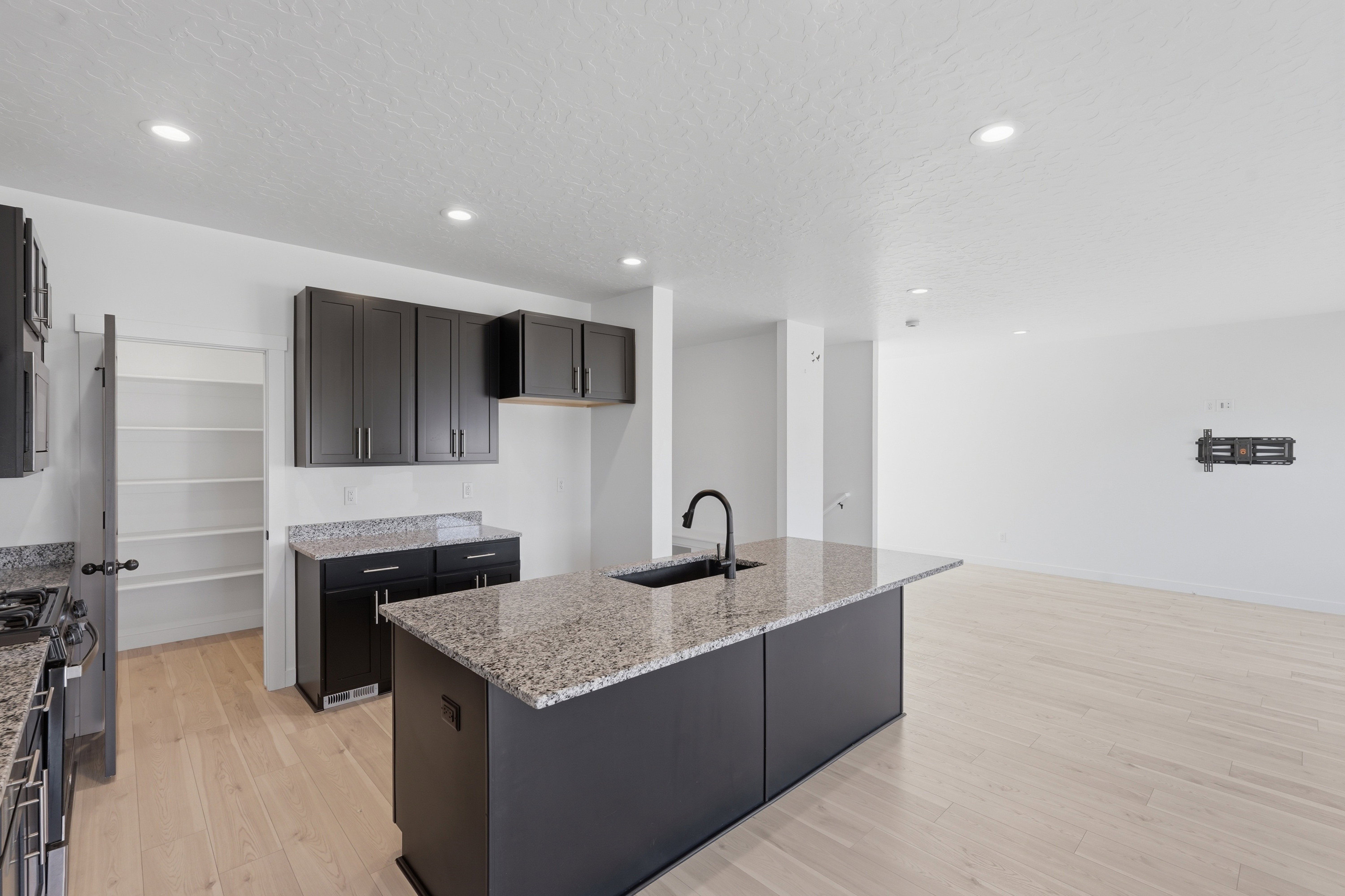 Modern kitchen featuring dark cabinetry, speckled countertops, a center island with an undermount sink, and light wood-finish flooring