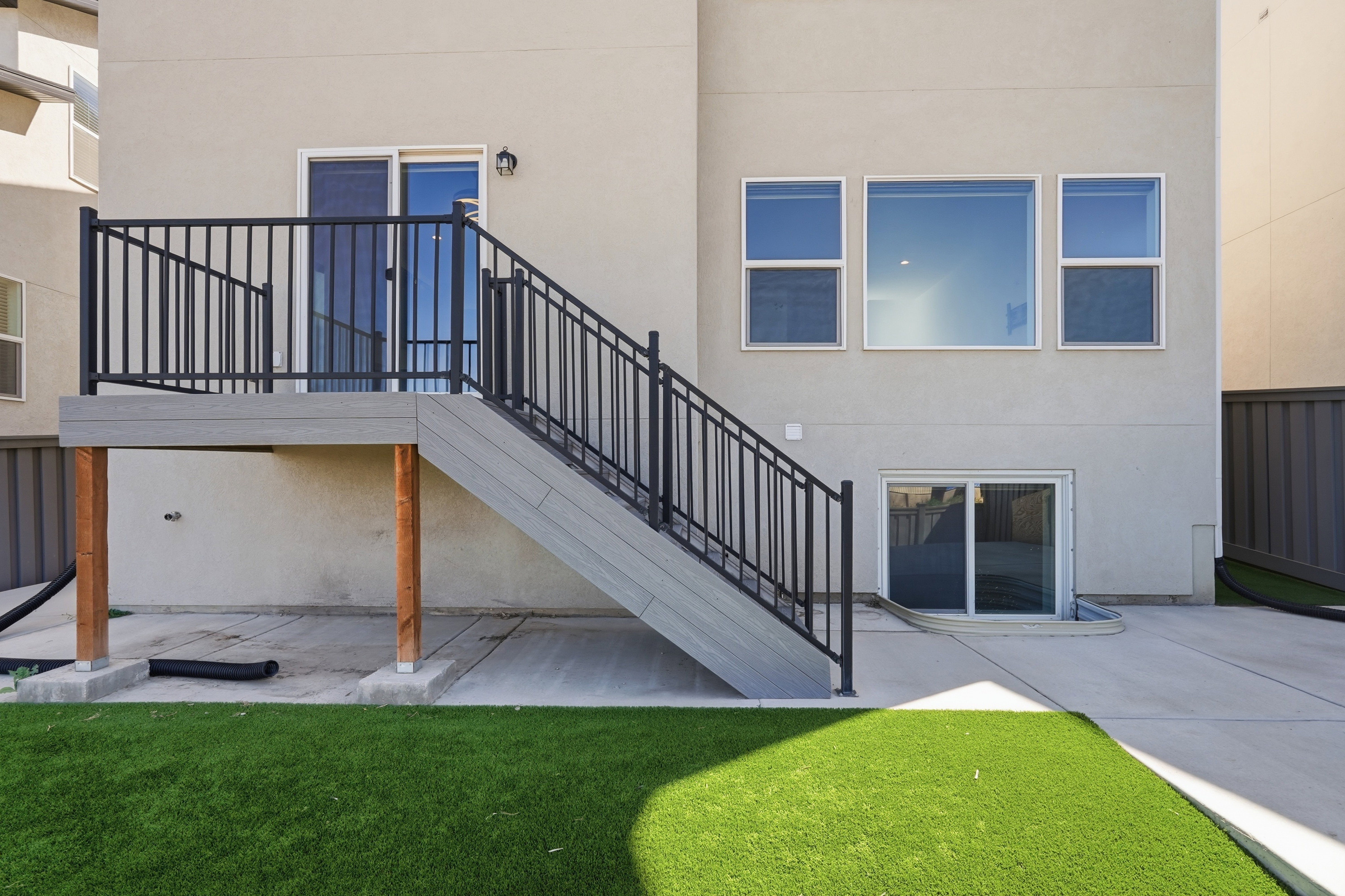 Rear exterior with a composite deck featuring black metal railings, a sliding glass door, and a lower-level concrete patio with a walk-out basement entrance